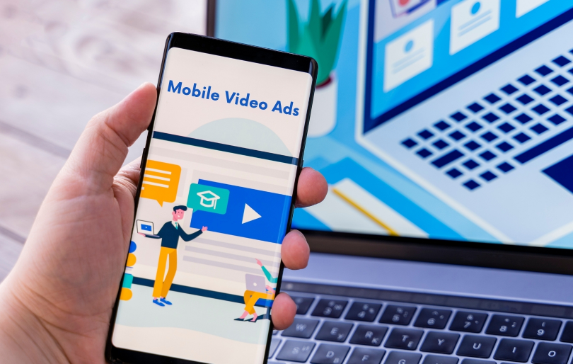 Hand Holding Mobile Phone and Laptop in Background